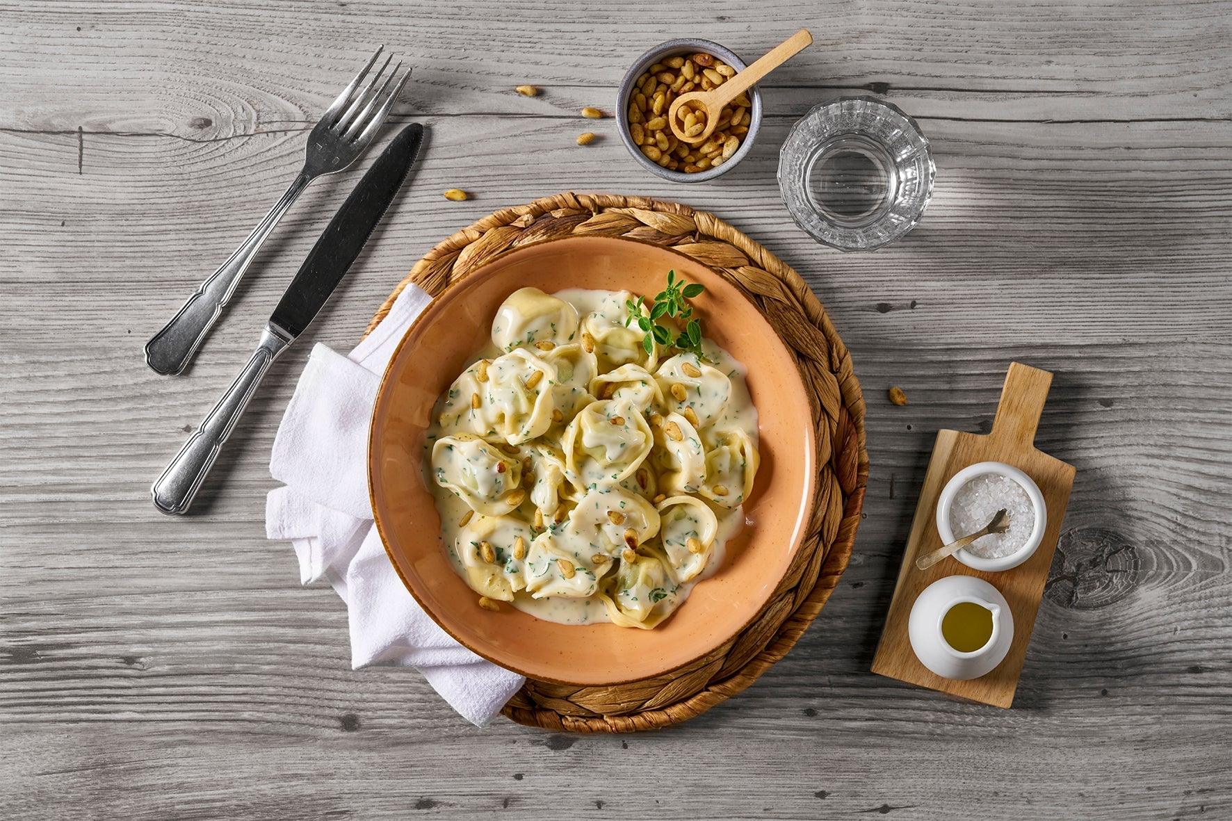 Eine Schale cremiger Tortellini aus der HOFMANNs Feinschmecker-Box auf einem rustikalen Holztisch.