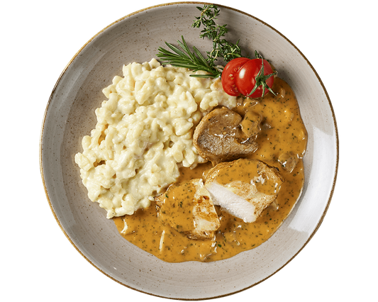 Ein Filetteller aus Hofmanns Shop mit cremigen Käsespätzle, Hähnchenbrustfiletscheiben in brauner Sauce, Kirschtomaten und Kräutern zum Garnieren.