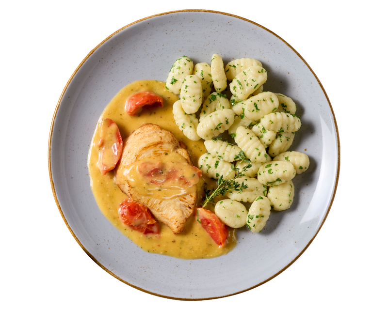 Sahne-Tomaten-Hähnchen von HOFMANNs mit Kräuter-Gnocchi auf einem grauen Teller.