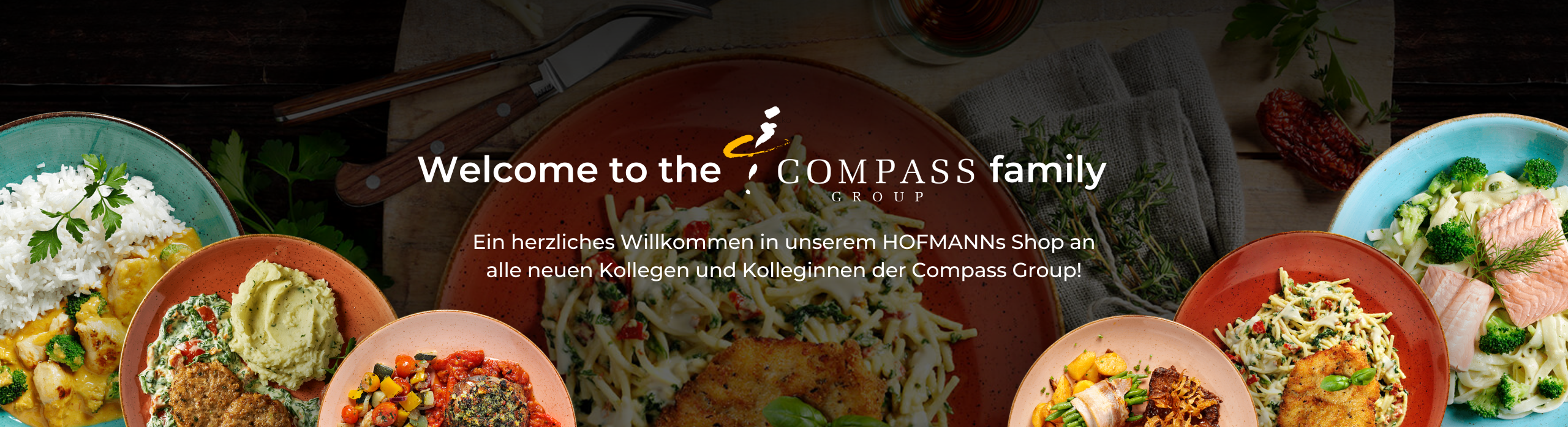 Willkommensschild der Compass Group mit verschiedenen Gerichten und einem deutschen Text zur Begrüßung neuer Kollegen.