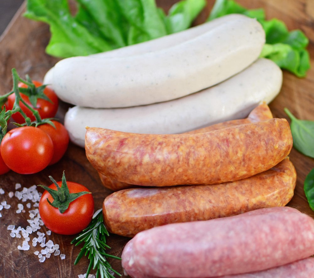 Verschiedene Würstchen mit Kirschtomaten, Salat und Salzkristallen auf einer Holzoberfläche.
