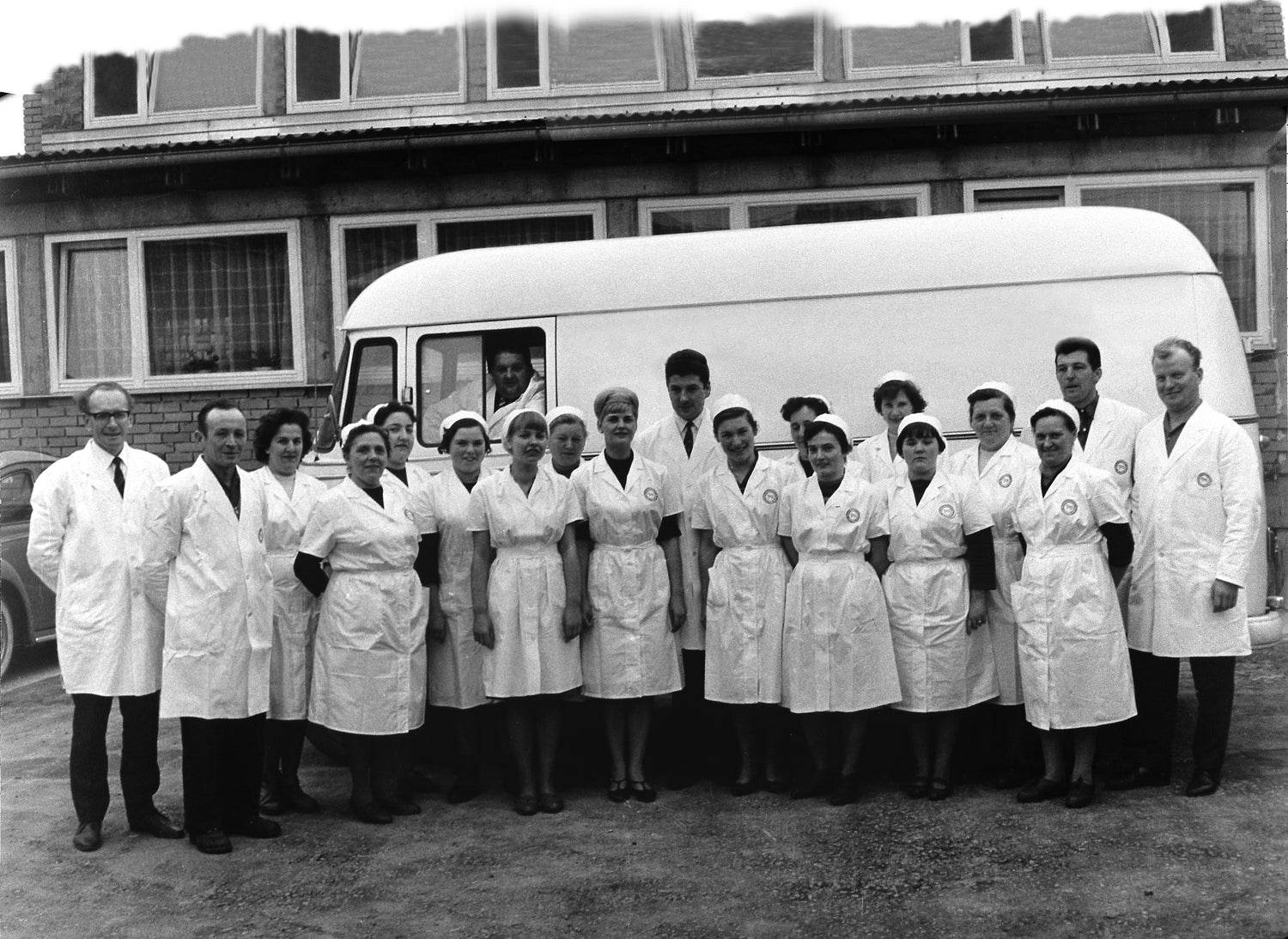 Eine Gruppe von Menschen in weißen Uniformen steht vor einem Lieferwagen und posiert vor einem Gebäude für ein Foto.