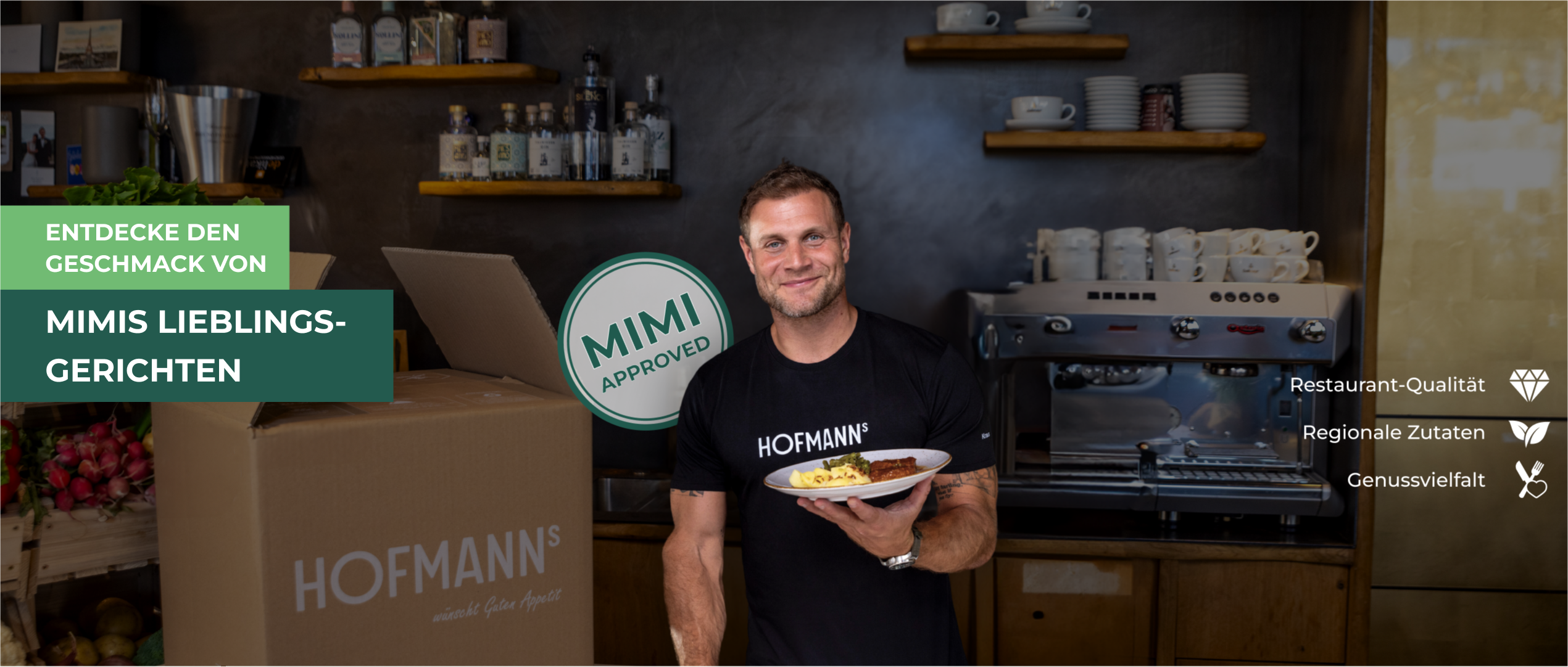 Lächelnder Mann hält in einer Küche einen Teller mit Essen, neben ihm eine große Schachtel mit dem „Mimi Approved“-Logo.