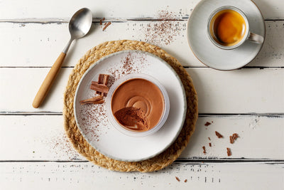 Eine Tasse Espresso und Mousse dunkel von Hofmanns Shop mit Schokoladenraspeln auf einem weißen Tisch.
