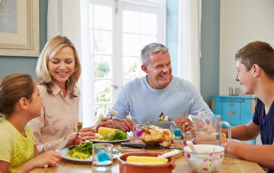 Eine vierköpfige Familie genießt eine fröhliche Mahlzeit an einem Esstisch in einem hellen Raum.