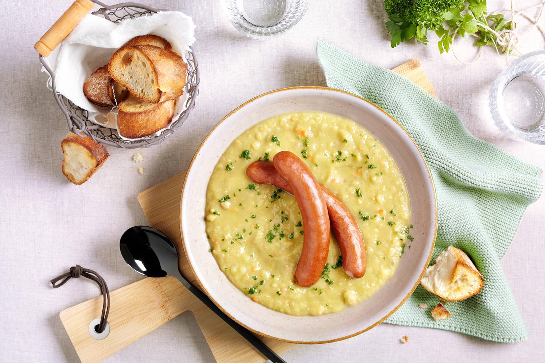 Eine cremig gelbe HOFMANNs Suppen & Eintöpfe mit Würstchen, Kräutern und Brot von HOFMANNs.