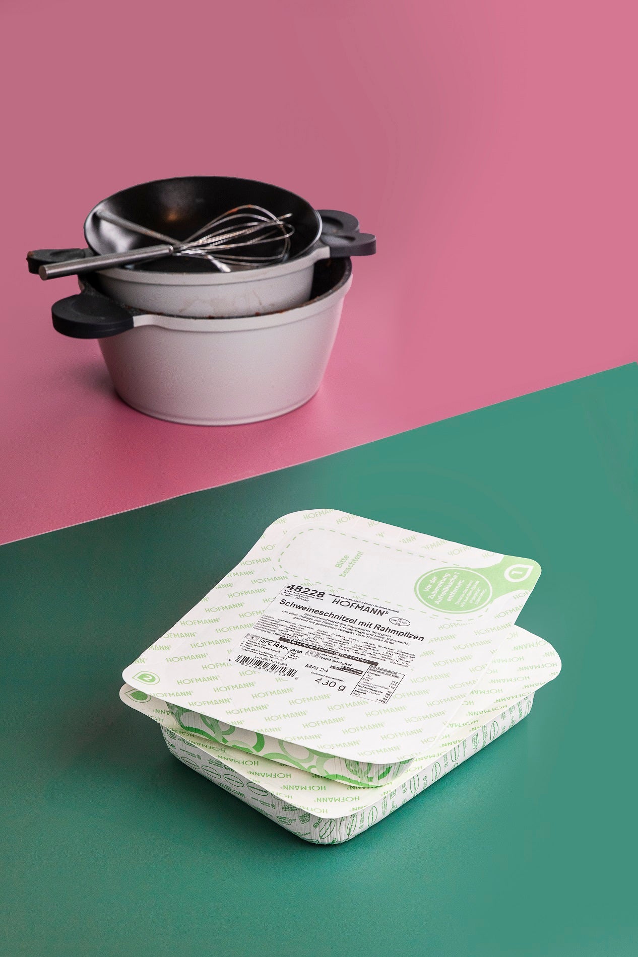 Im Hintergrund gestapelte schmutzige Schüsseln und Schneebesen und abgepackte Lebensmittel auf einer zweifarbigen rosa-grünen Oberfläche.
