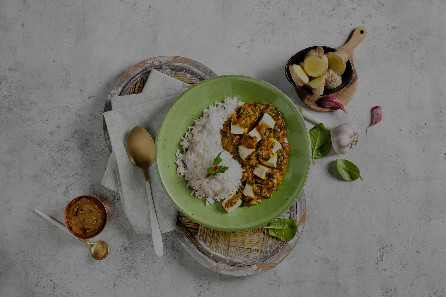 Eine grüne Schüssel mit Reis und Paneer-Curry aus HOFMANNs Mikrowellen-Genuss-Box auf grauem Untergrund.