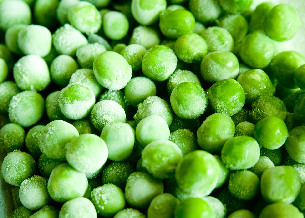 Nahaufnahme von leuchtend grünen Tiefkühlerbsen mit Frostüberzug.