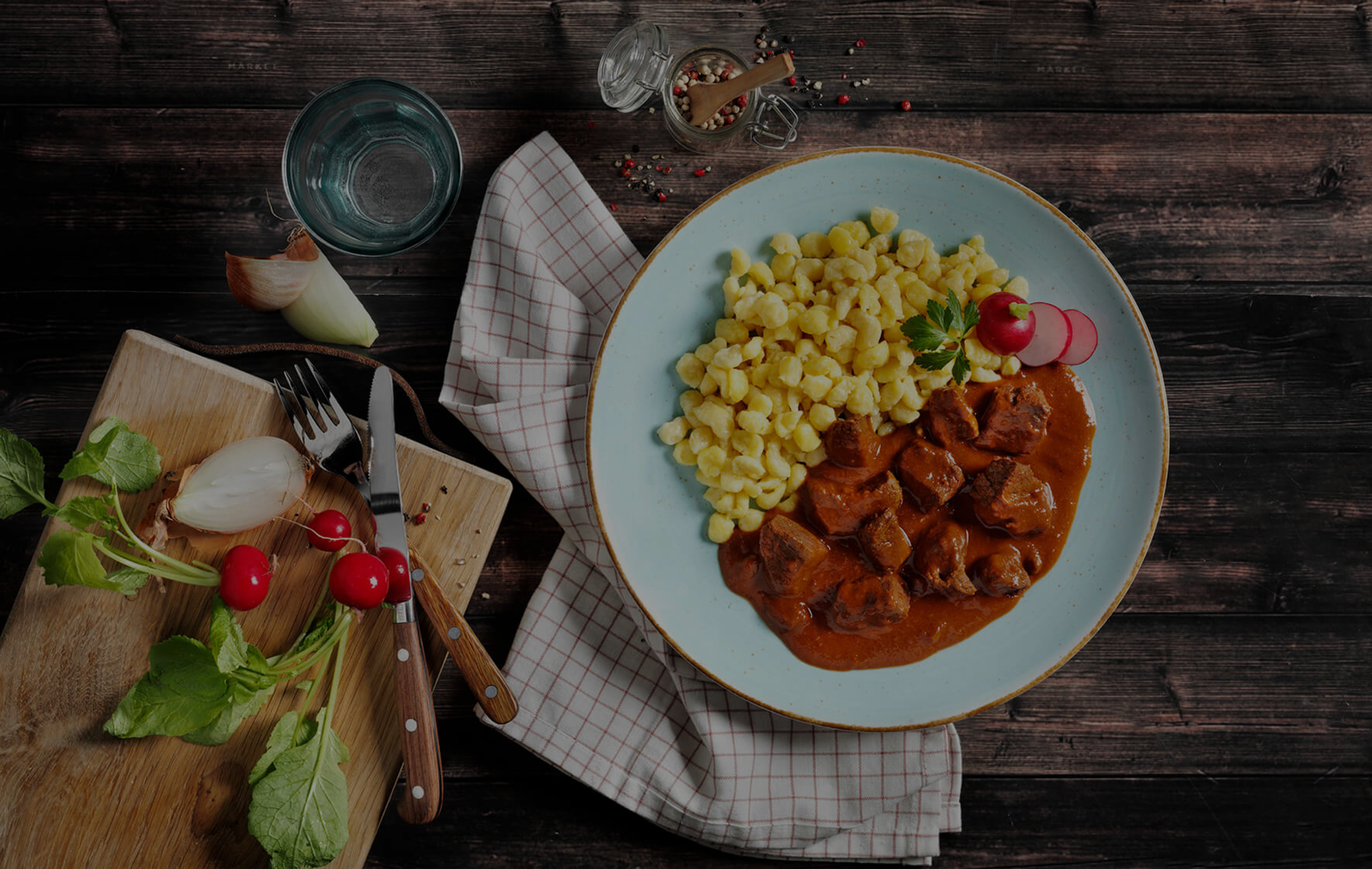 Eine herzhafte Mahlzeit aus Nudeln und Fleisch in Tomatensoße mit frischem Gemüse, serviert auf einem Teller mit Besteck in der Nähe.