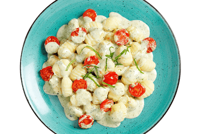 Hofmanns Shop Gnocchi à la Caprese mit Kirschtomaten und Basilikumsauce, serviert auf einem blauen Teller.