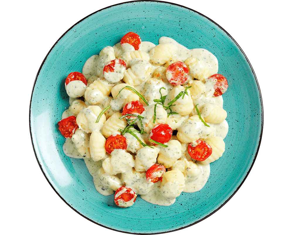 Hofmanns Shop Gnocchi à la Caprese mit Kirschtomaten und Basilikumsauce, serviert auf einem blauen Teller.