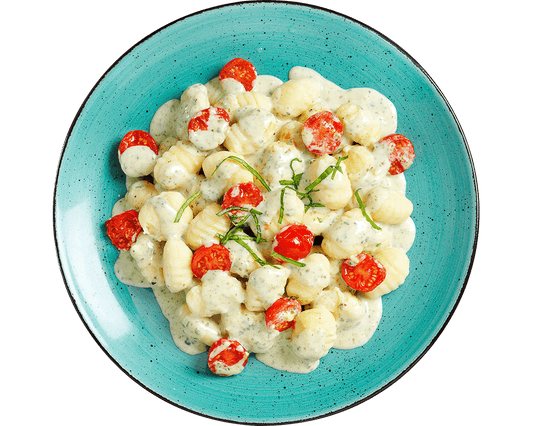 Hofmanns Shop Gnocchi à la Caprese mit Kirschtomaten und Basilikumsauce, serviert auf einem blauen Teller.