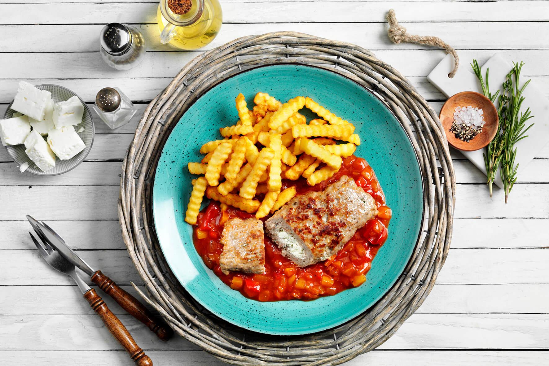 Blauer Teller mit Hofmanns Shop Hackroulade „Griechische Art“, Crinkle Pommes und Tomatensoße.