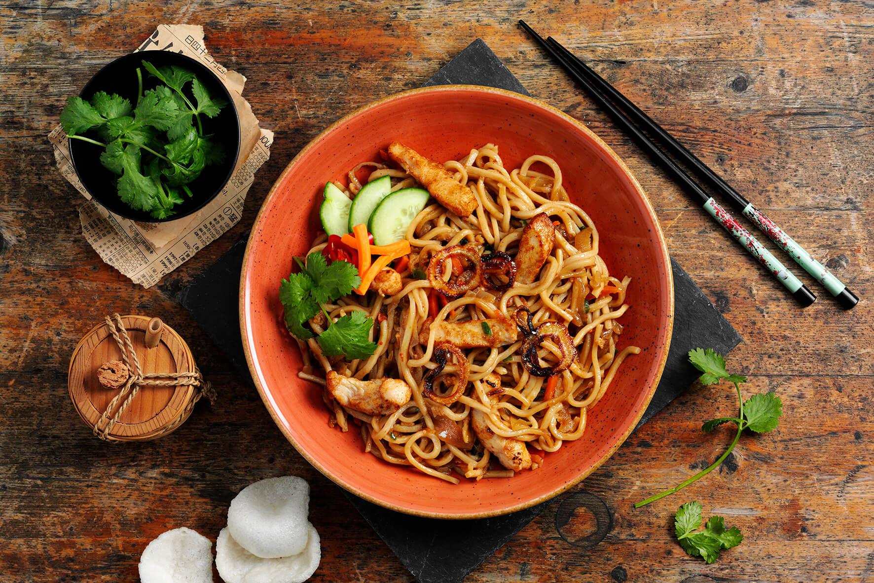 Hofmanns Shop Bami Goreng, gebratene Hühnernudelsuppe nach indonesischer Art, mit Koriander und Stäbchen.