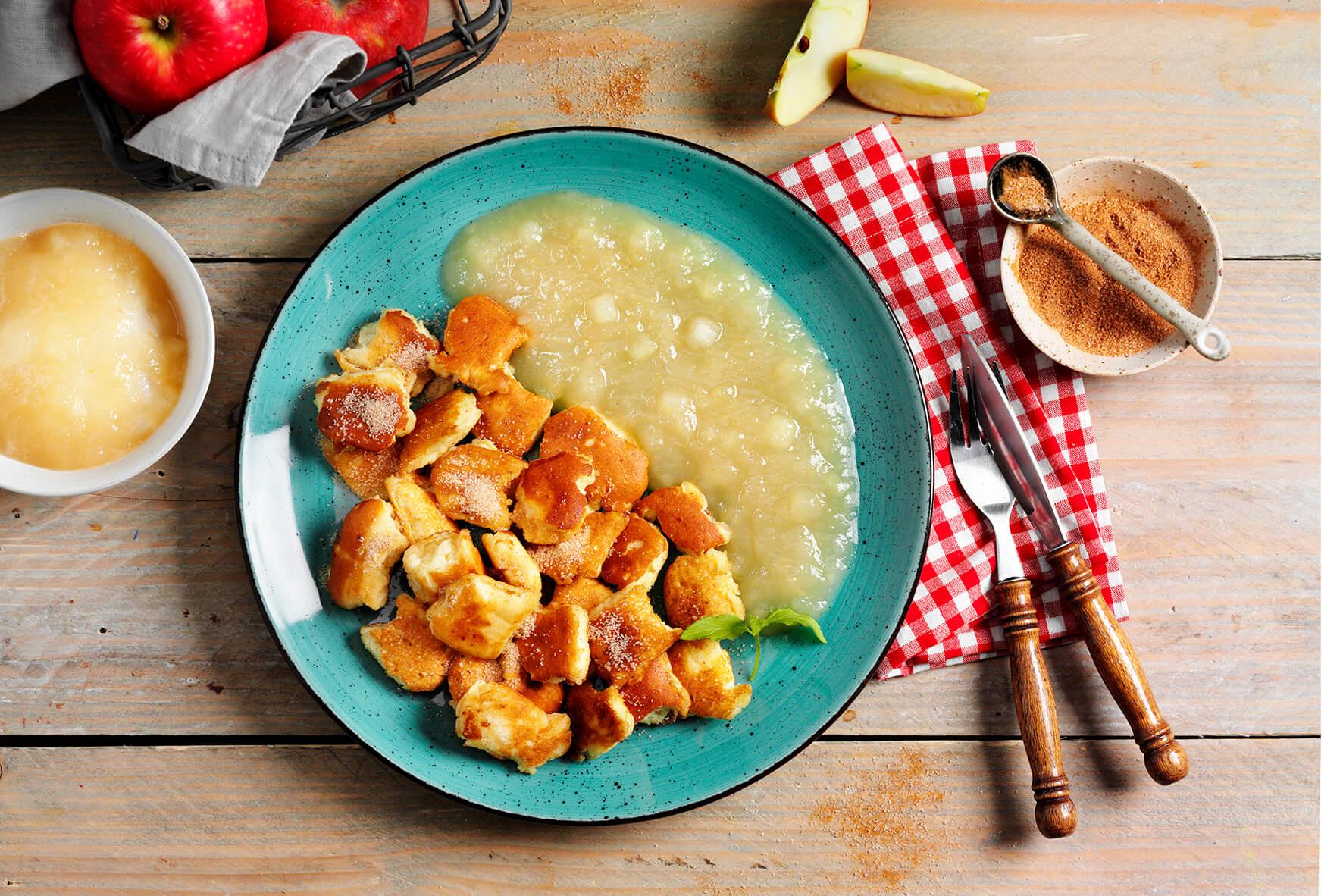Ein Teller von Hofmanns Shop Kaiserschmarrn mit Apfelkompott mit Äpfeln, Besteck und einer rotkarierten Serviette.