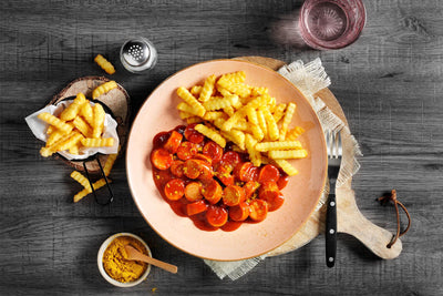 Ein Teller Hofmanns Shop Currywurst „Hot Chili“ mit extra Pommes und Madras-Curry-Gewürz.