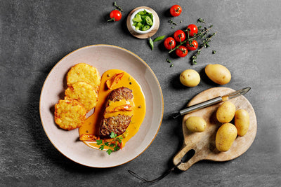 Teller mit Hofmanns Shop Hacksteak „Gipfelstürmer“, Sauce, Rösti, Tomaten, Kräutern und Kartoffeln.