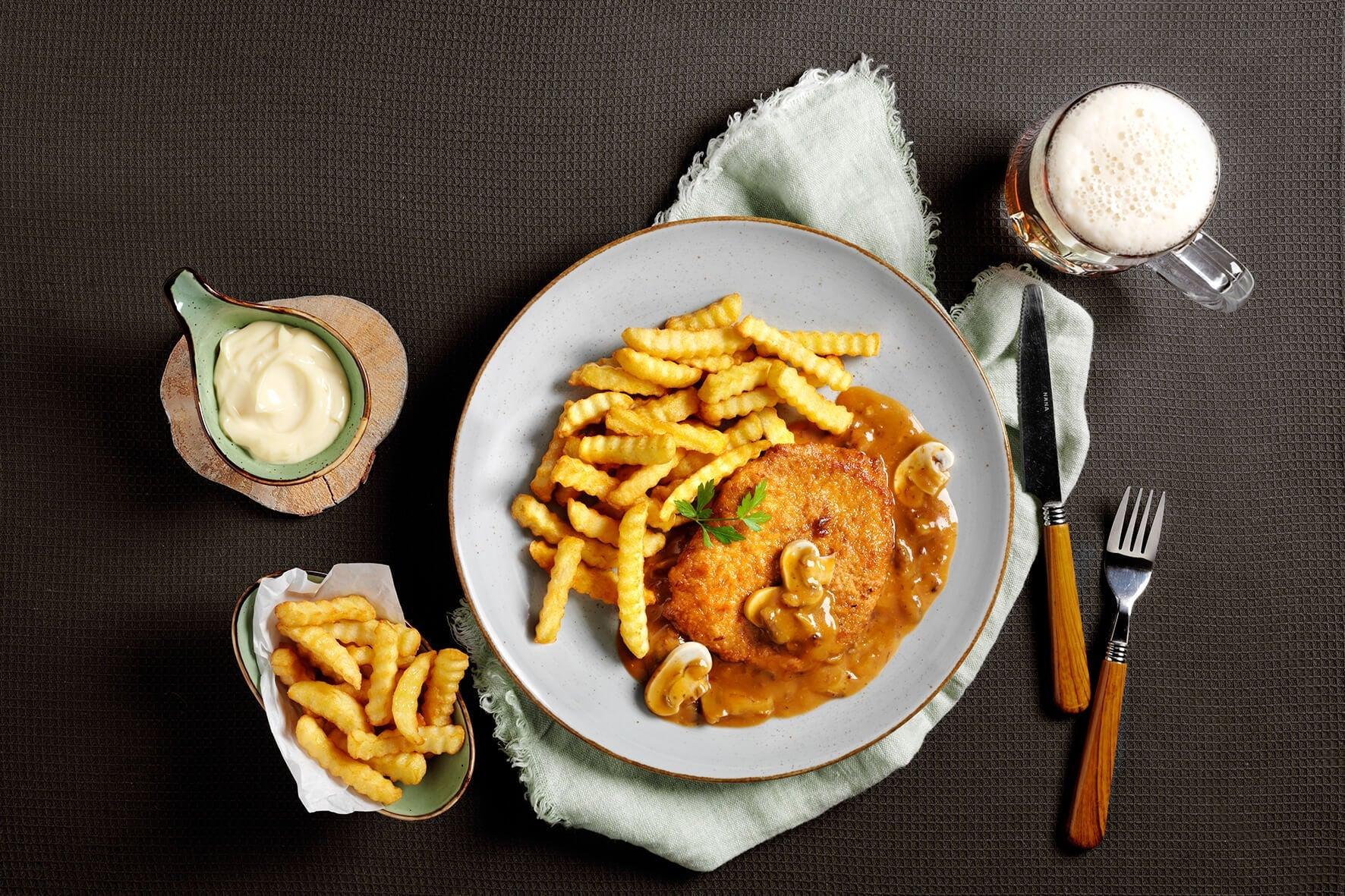 Jägerschnitzel von Hofmanns Shop, Wellenpommes, extra Pommes und ein Krug Bier auf dem Tisch.
