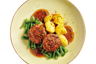 Zwei Hofmanns Shop Pfefferfrikadellen mit brauner Sauce, grünen Bohnen und Salzkartoffeln auf einem Teller.