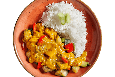 Ein Teller weißer Reis mit Rote-Linsen-Curry von Hofmanns Shop, Gemüse und geschnittenen Frühlingszwiebeln obendrauf.
