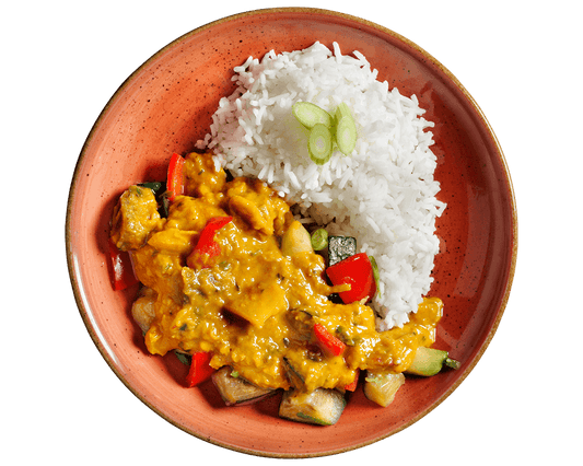 Ein Teller weißer Reis mit Rote-Linsen-Curry von Hofmanns Shop, Gemüse und geschnittenen Frühlingszwiebeln obendrauf.