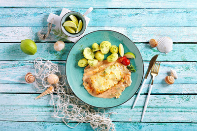 Schlemmerfilet alla Napoli von Hofmanns Shop, serviert mit Kartoffeln auf einem blauen Teller mit maritimem Dekor.