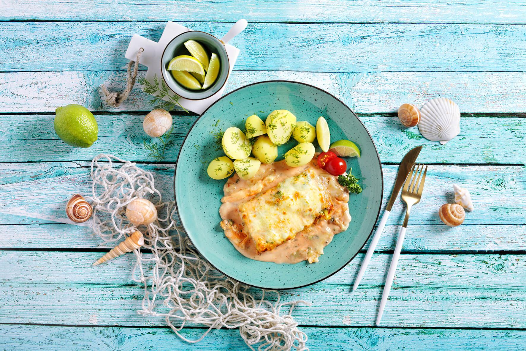 Schlemmerfilet alla Napoli von Hofmanns Shop, serviert mit Kartoffeln auf einem blauen Teller mit maritimem Dekor.