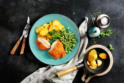 HOFMANNs Schnitzel-Box: paniertes Hähnchen, grüne Bohnen und Bratkartoffeln, Besteck liegt bereit.