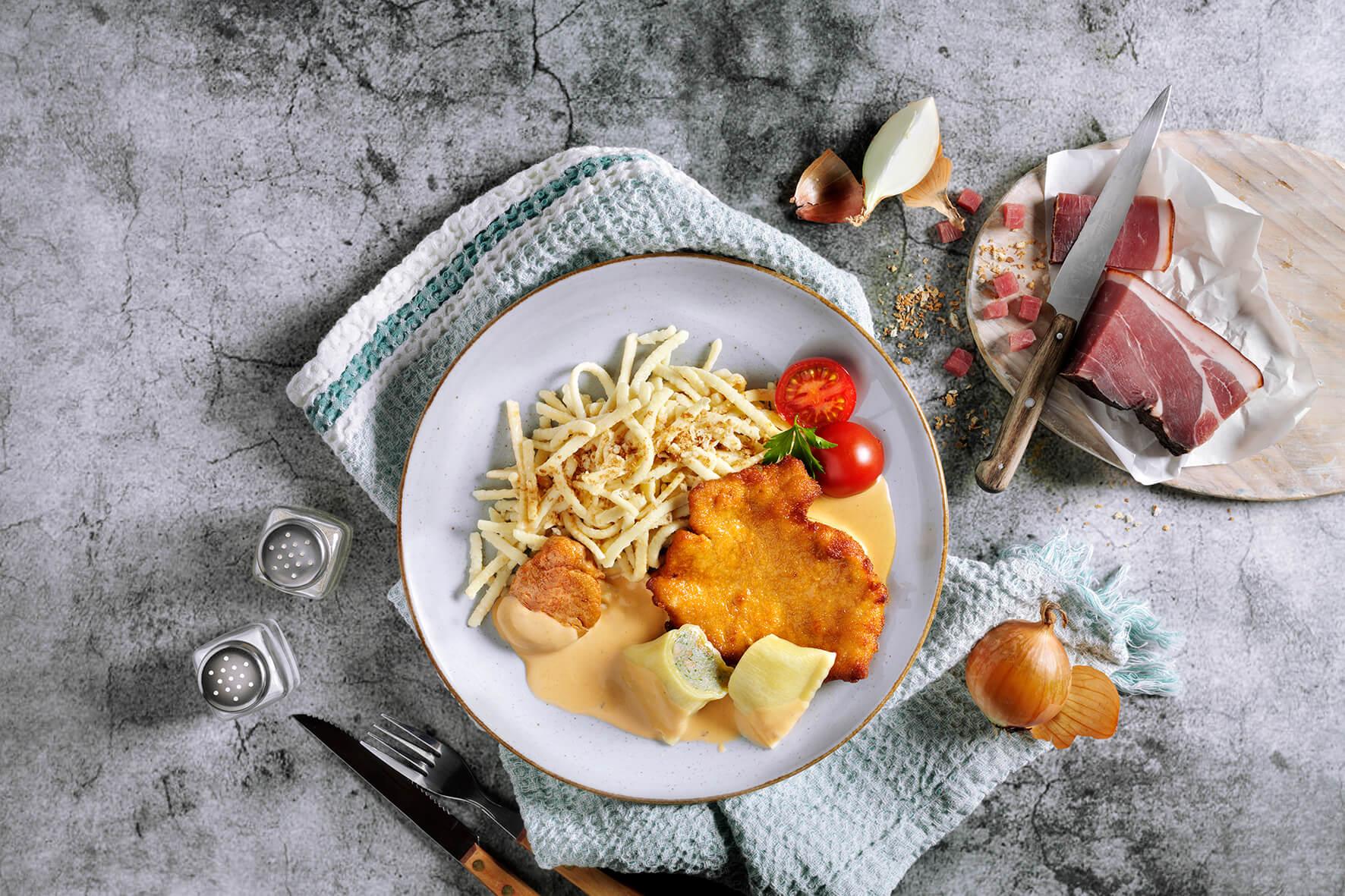 Hausmannskost-Box von HOFMANNs: Teller mit Schnitzel, Pommes, Soße, Tomate; Rinderrouladenseite.