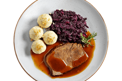 Zarter Sauerbraten von Hofmanns Shop mit Bratensoße, Apfelrotkohl und 3 Kartoffelklöße auf einem Teller.